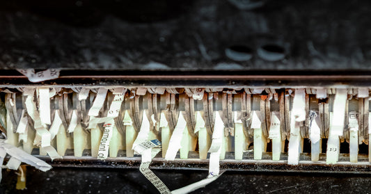 A close-up of industrial paper shredder blades. There are thin scraps of paper with text torn between the blades.