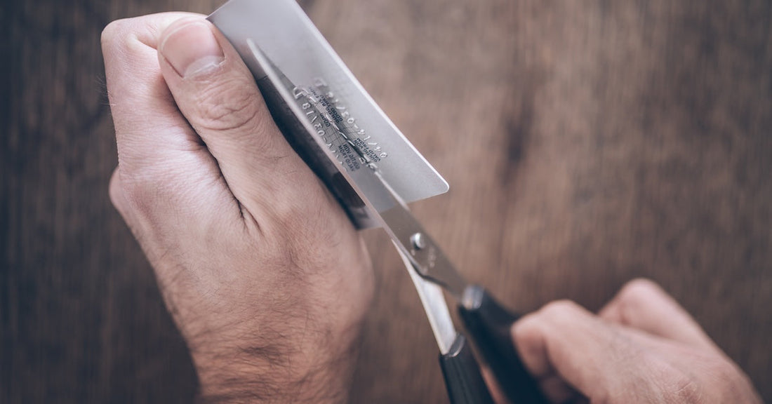 A person using a pair of scissors to cut a white, plastic card. They are slicing the card in half, longways.