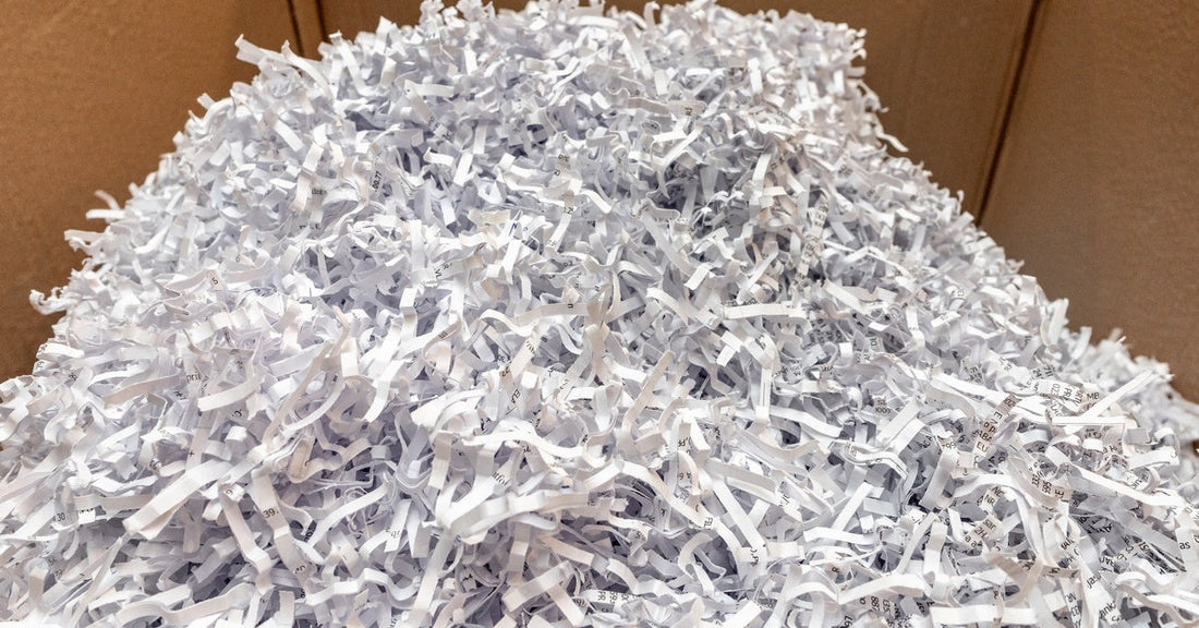 Strips of shredded paper with undistinguishable text are in a tall pile. They're placed inside of a large cardboard box.