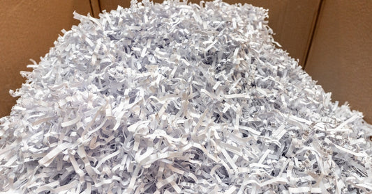 Strips of shredded paper with undistinguishable text are in a tall pile. They're placed inside of a large cardboard box.