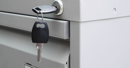 A close-up of a gray file cabinet with a lock positioned on the cabinet's frame. A key is twisted into the lock.