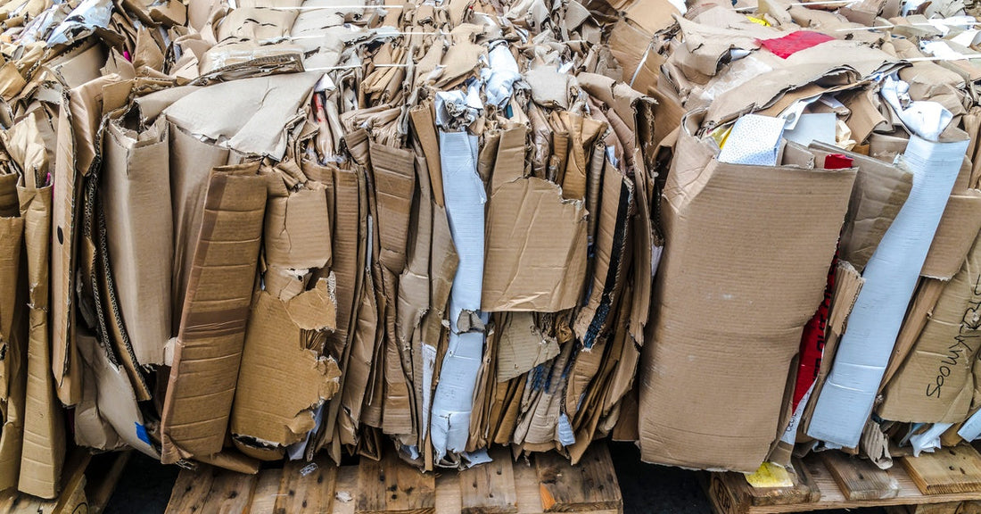 A stacked bale of flattened cardboard boxes sits on wooden pallets with torn edges and mixed paper scraps.
