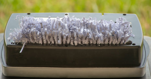 Shredded paper scraps overflowing the top of a paper shredder machine. The scraps are sliced into strips.