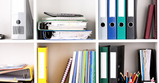 A bookshelf filled with folders, binders, and pencils. Some items are laying flat, while others are leaning against the wall.