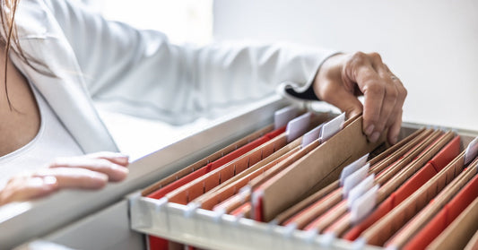 A person wearing white clothes grabs a folder from a drawer that's full of tan and red folders with white tabs.