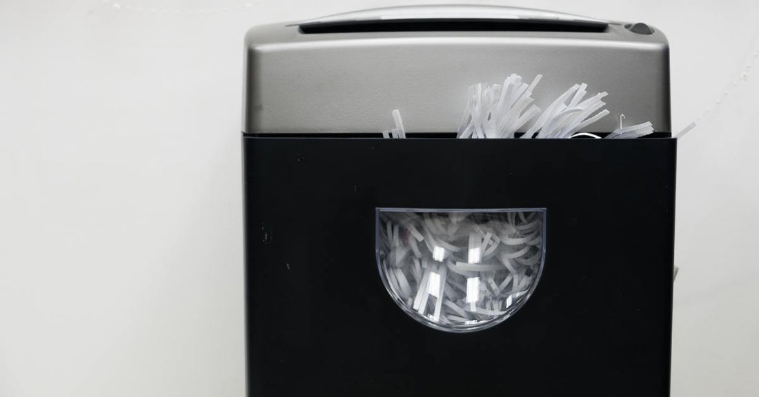 A close-up of a black and gray paper shredder. The bin of the shredder has a window that's full of strips of paper.