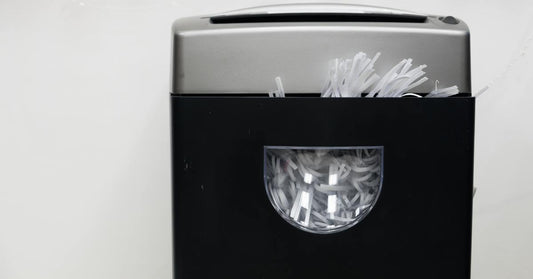 A close-up of a black and gray paper shredder. The bin of the shredder has a window that's full of strips of paper.