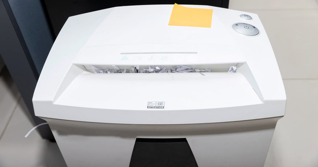 An overhead view of a white paper shredder. There are strip-cut shreds of paper stuck in the feed opening.