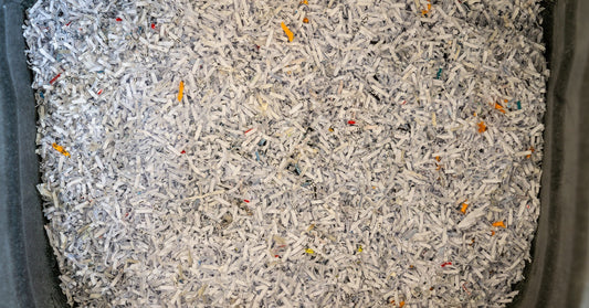 A close-up of white and yellow shredded strips of paper are in a large, gray bin that fills the frame.