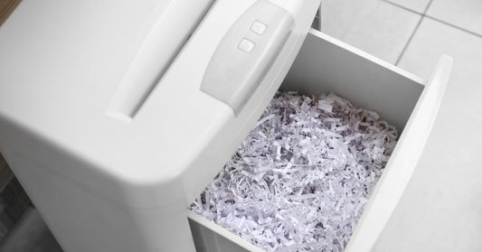 An overhead view of a white document shredder with an open bin. The bin is full of small shreds of paper.