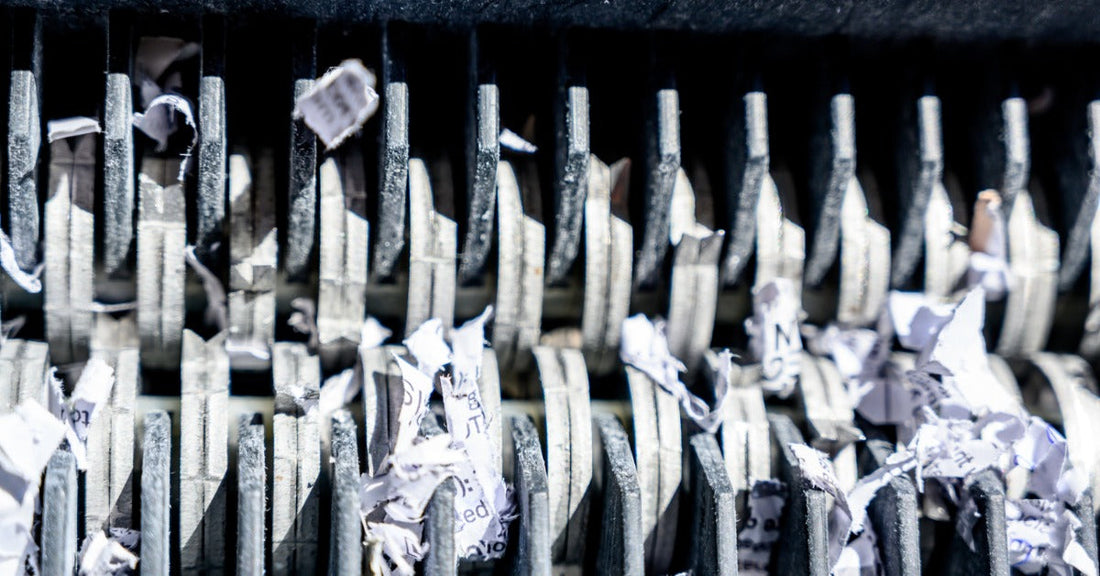 An extreme close-up of the cutting blades of a paper shredder. Cross-cut sheds of paper are in between the blades.