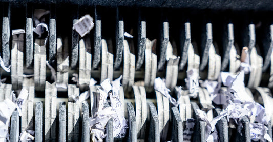 An extreme close-up of the cutting blades of a paper shredder. Cross-cut sheds of paper are in between the blades.