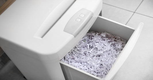 A white paper shredder filled with strips of paper in its compartment. The paper shredder is sitting on white tile floor.