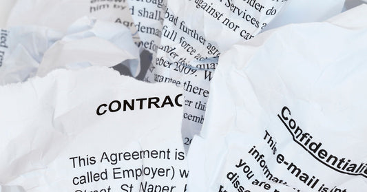 Scraps of ripped-up paper with black text written on them that reads "Contract" and "Confidential." The papers sit in a pile.