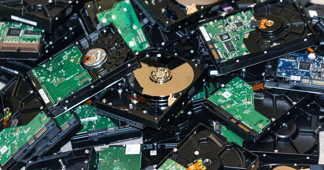 A pile of opened computer hard drives showing green circuit boards, black casings, and exposed metal storage disks.